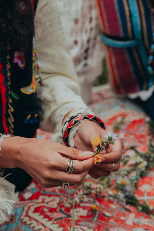 a close up of a person holding a flower, tribal clothing, herbs and flowers, bracelets, reaching out to each other