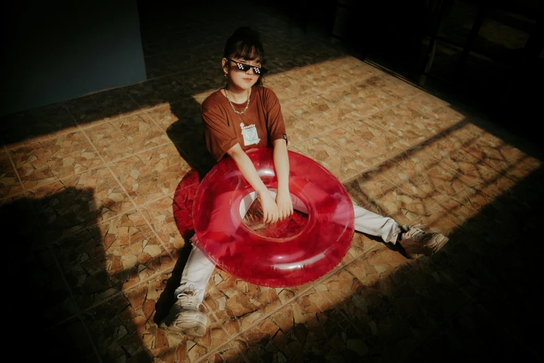 a young boy sitting on top of a red frisbee, by Nathalie Rattner, pexels contest winner, girl wearing round glasses, sun yunjoo, sitting on the floor, extreme drama