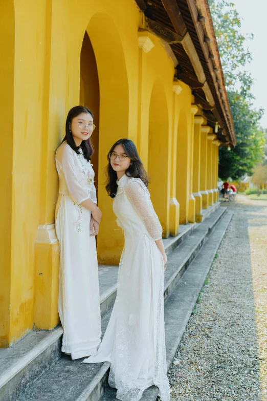 a couple of women standing next to each other, inspired by Cui Bai, unsplash, renaissance, ao dai, white and yellow scheme, delightful surroundings, portrait image