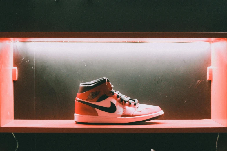 a pair of sneakers sitting on top of a shelf, inspired by Jordan Grimmer, trending on unsplash, hyperrealism, red rim light, orange and black, air jordan 1 high, sunfaded