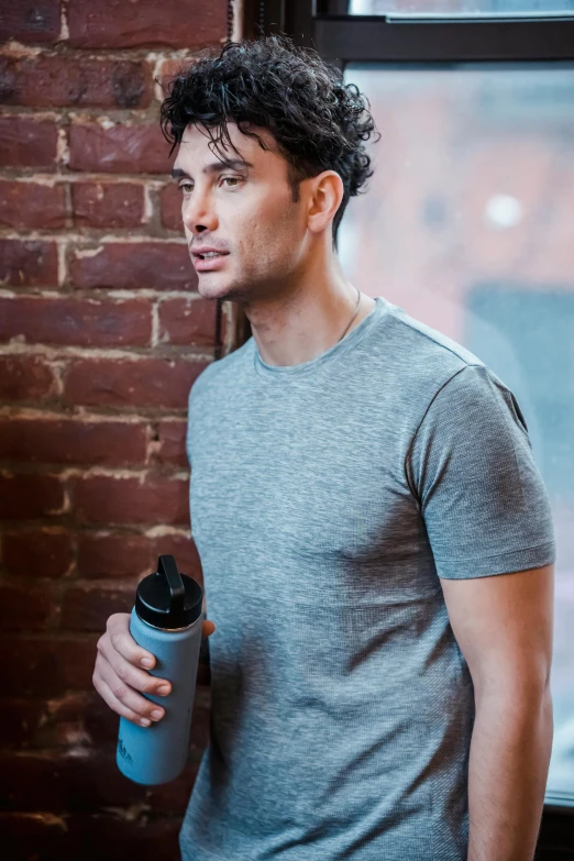 a man standing in front of a window holding a water bottle, a portrait, inspired by John Luke, shutterstock, wearing tight shirt, in gunmetal grey, walking to the right, medium close-up shot