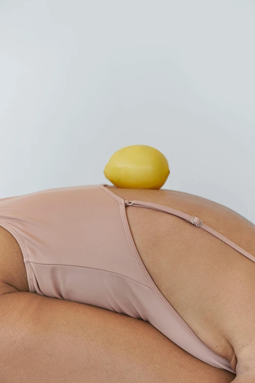 a woman laying on a bed with a lemon on top of her stomach, inspired by Sarah Lucas, unsplash, renaissance, silicone skin, showing her shoulder from back, holding a ball, detailed product shot