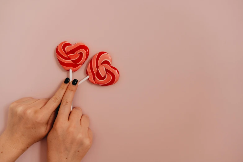 a person holding two lollipops in their hands, inspired by Louise Bourgeois, trending on pexels, soft red texture, candy land, background image, 👅 👅