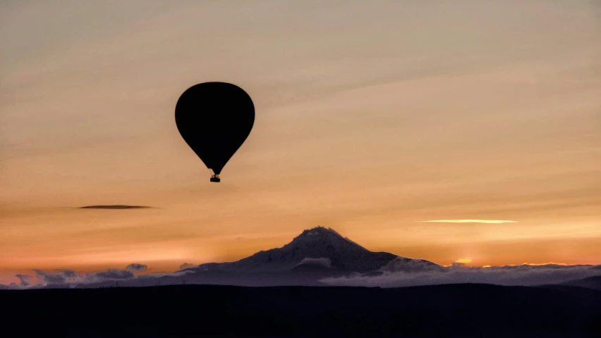 a hot air balloon flying over a mountain at sunset, by Peter Churcher, black volcano afar, black silhouette, ballard, distant photo