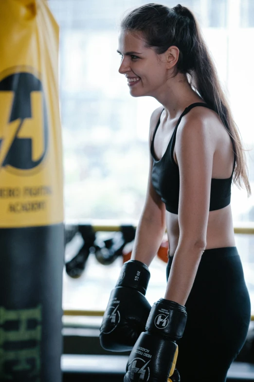 a woman standing next to a punching bag, black and yellow, wearing fitness gear, malaysian, wētā fx
