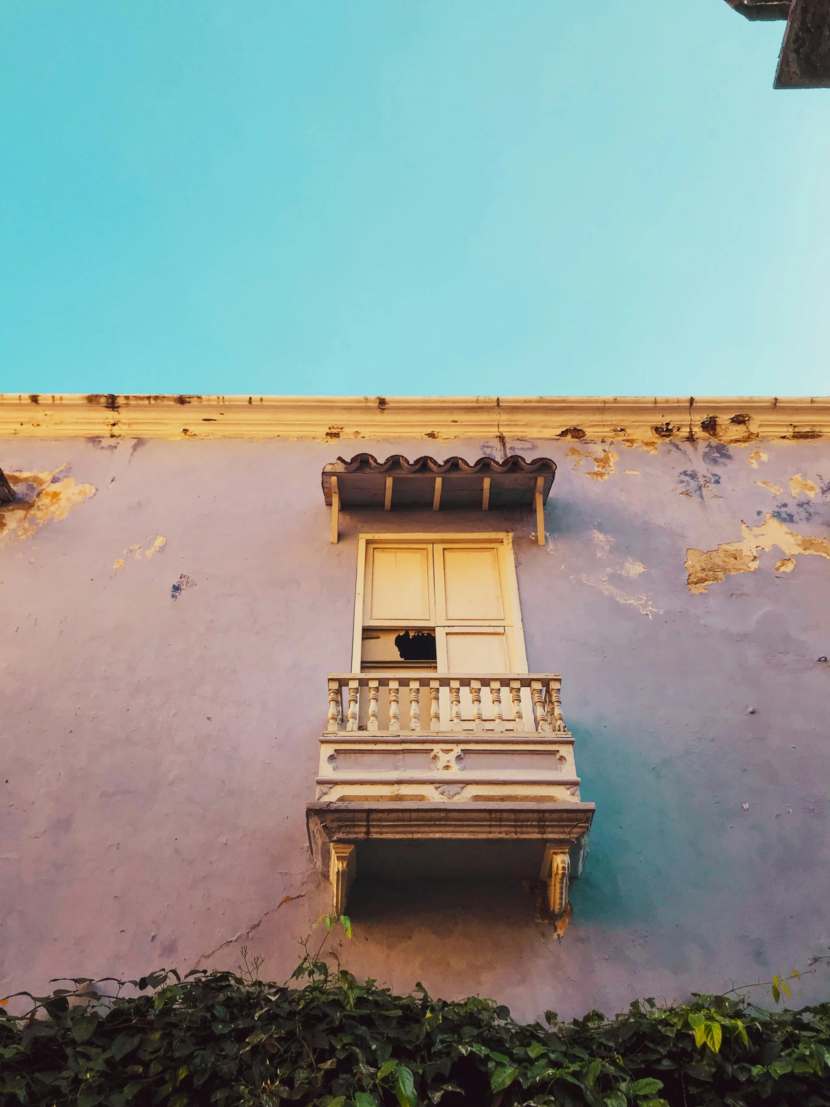 a building with a balcony in front of a blue sky, inspired by Fede Galizia, pexels contest winner, yellow and purple tones, faded glow, tlaquepaque, medium format color photography