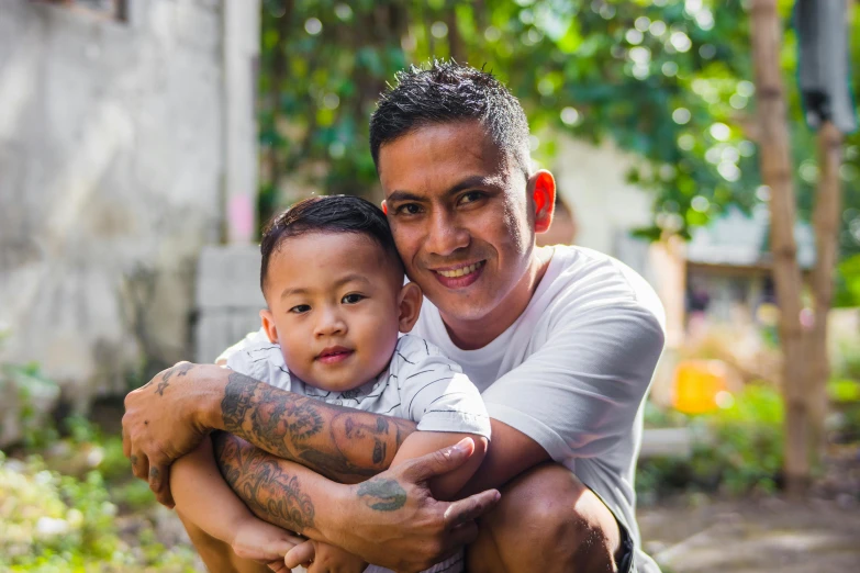 a man holding a small child in his arms, pexels contest winner, sumatraism, avatar image, tattooed, confident looking, south east asian with round face