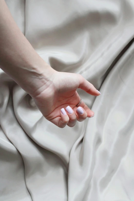 a close up of a person's hand on a bed, inspired by Anna Füssli, soft silk dress, matte material, iridiscent fabric