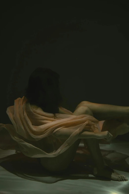 a woman sitting on a bed in the dark, inspired by Elsa Bleda, floating bodies, wet fabric, on a table, showstudio