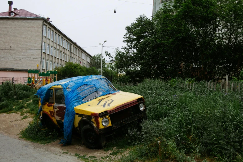 a car covered in plastic sitting on the side of a road, by Sven Erixson, unsplash, auto-destructive art, soviet apartment buildings, overgrown with weeds, 000 — википедия, a wooden
