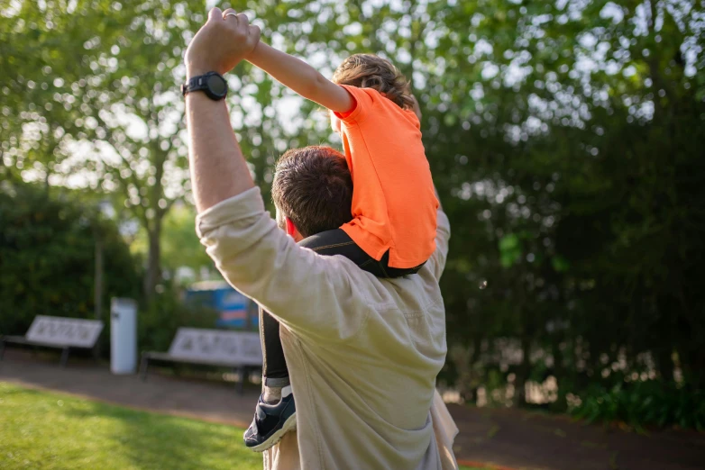 a man holding a child up in the air, orange safety vest, walking at the park, orange shoulder pads, wearing hi vis clothing