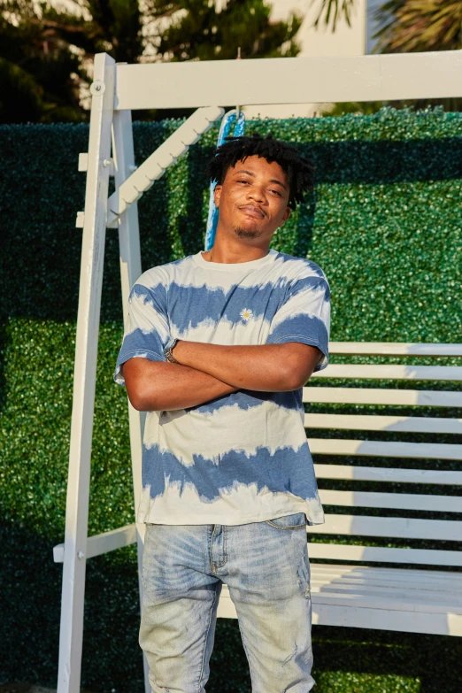 a man standing in front of a white swing, renaissance, wearing a tie-dye t-shirt, in style of tyler mitchell, breezy background, official store photo