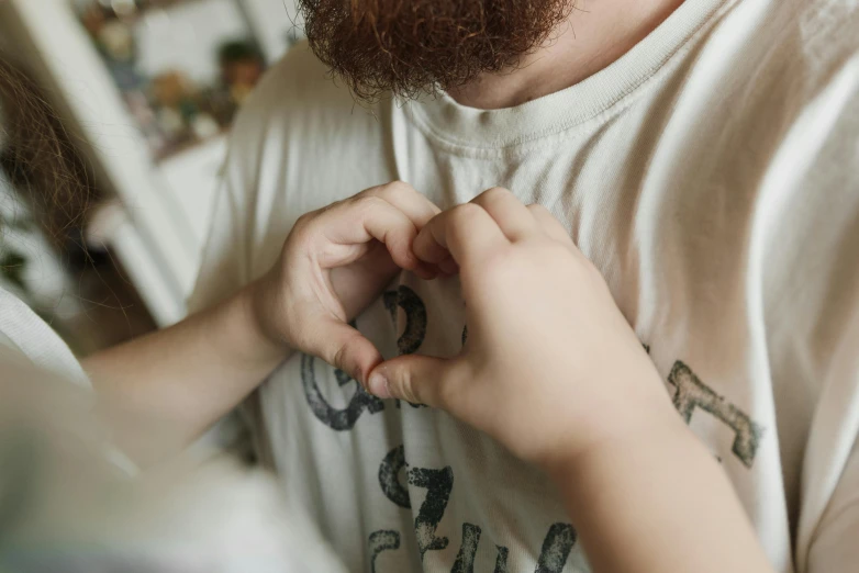 a man making a heart with his hands, trending on pexels, embroidered shirt, reddish beard, nursing, t - shirt