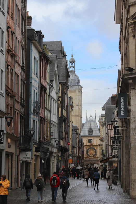 a group of people walking down a street next to tall buildings, a photo, inspired by Pierre Toutain-Dorbec, renaissance, medieval town, clock tower, normandy, temples