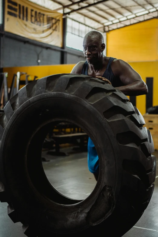 a man holding a large tire in a gym, a portrait, pexels contest winner, black man, pulling the move'derp banshee ', heavy machinery, profile image