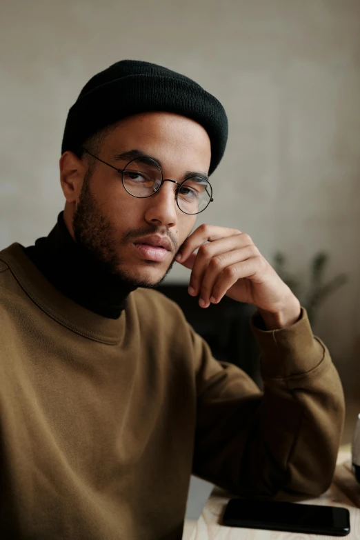 a man sitting at a table with a cell phone, a character portrait, trending on pexels, square rimmed glasses, wearing turtleneck, ready to model, riyahd cassiem