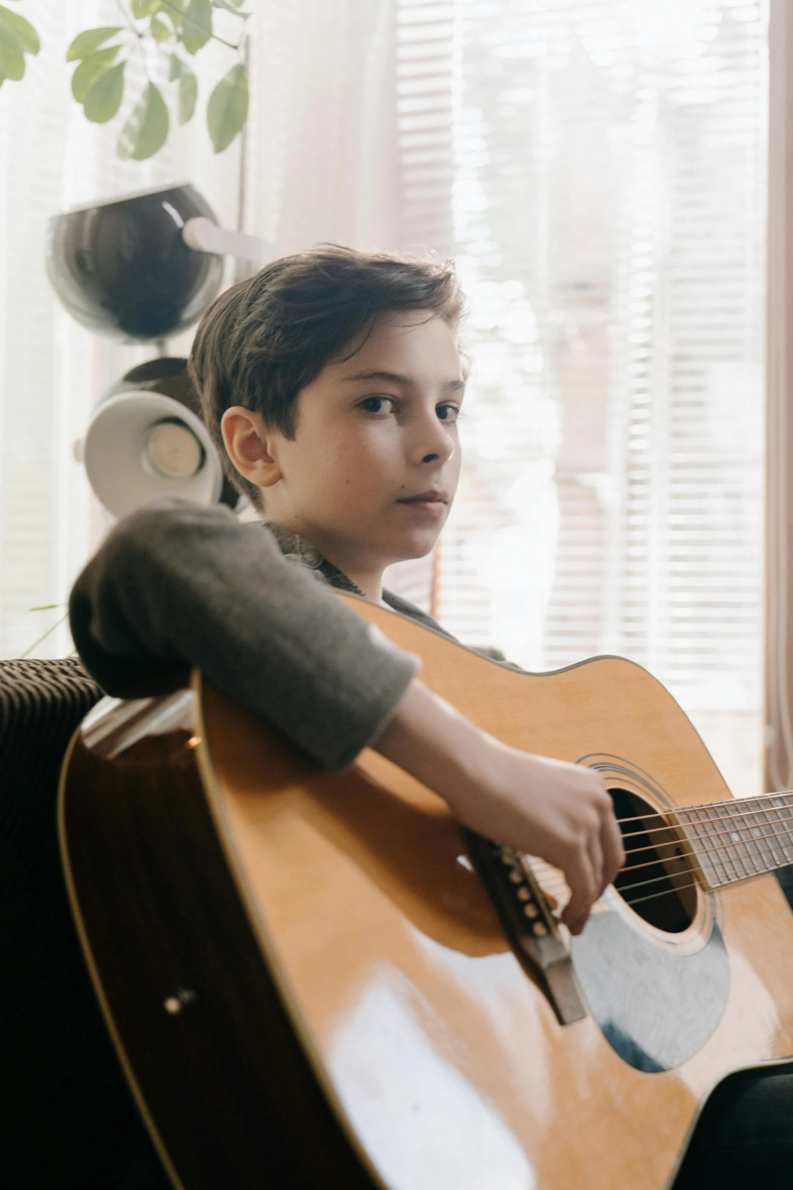 a boy sitting on a couch playing a guitar, looking off to the side, jen atkin, compassionate, song