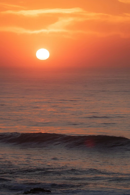 a person riding a surfboard on top of a wave, during a sunset, sunset in the distance, hollister ranch, red sun