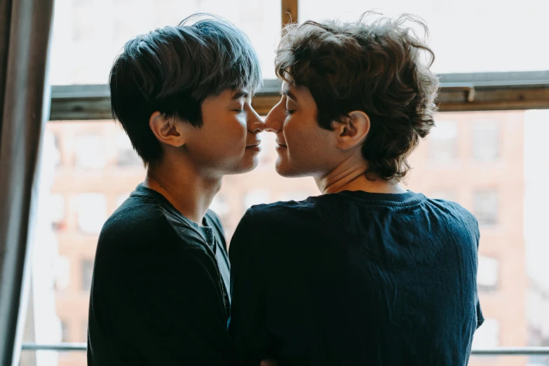 a couple of people standing in front of a window, pexels contest winner, realism, lesbian kiss, zeen chin and terada katsuya, profile image, he has short curly brown hair