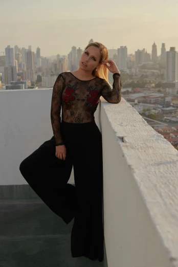 a woman standing on top of a building with a city in the background, inspired by Amelia Peláez, arabesque, wearing black modern clothes, wearing a designer top, jumpsuit, profile image