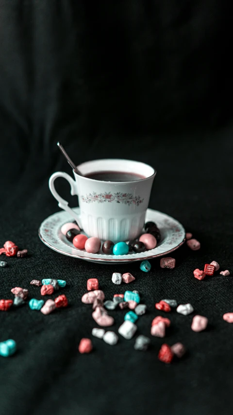 a cup of coffee sitting on top of a saucer, a colorized photo, inspired by Wlodzimierz Tetmajer, pexels contest winner, candy decorations, black rococo, jellybeans, with a long