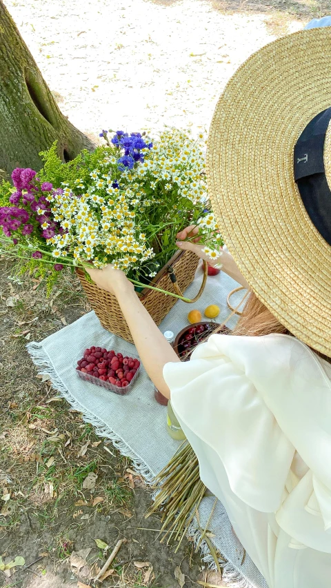 a woman sitting under a tree with a basket of flowers, pexels, with straw hat, berries, top down shot, recipe