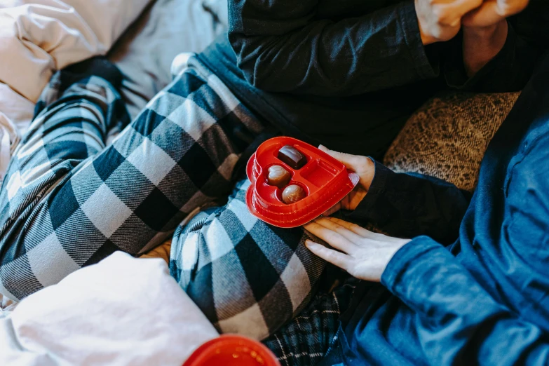 a couple of people sitting on top of a bed, trending on pexels, having a snack, red sweater and gray pants, hearts, game ready
