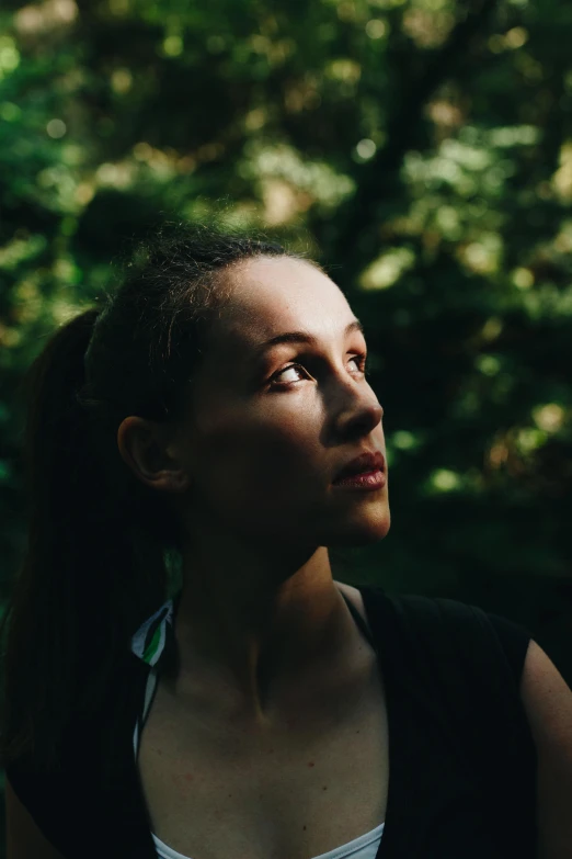 a woman standing in front of a lush green forest, a portrait, by Adam Marczyński, profile image, sun lighting, looking serious, multiple stories