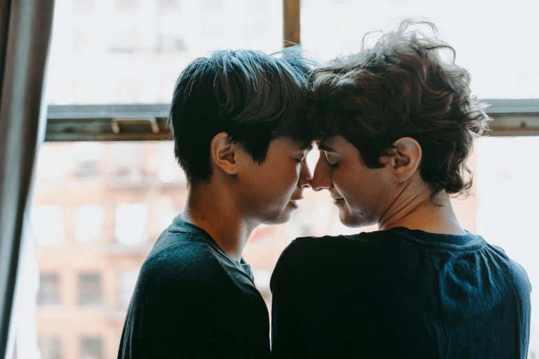 a couple standing next to each other in front of a window, by Nina Hamnett, trending on pexels, queer woman, facing each other, touching heads, rebecca sugar