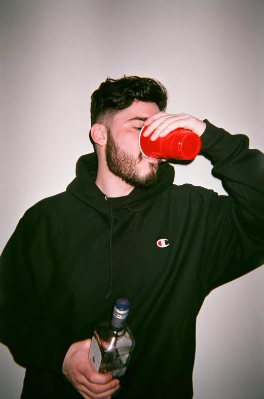 a man in a black hoodie drinking from a bottle, an album cover, inspired by Ion Andreescu, trending on pexels, ((red)) baggy eyes, college party, profile picture 1024px, half bear