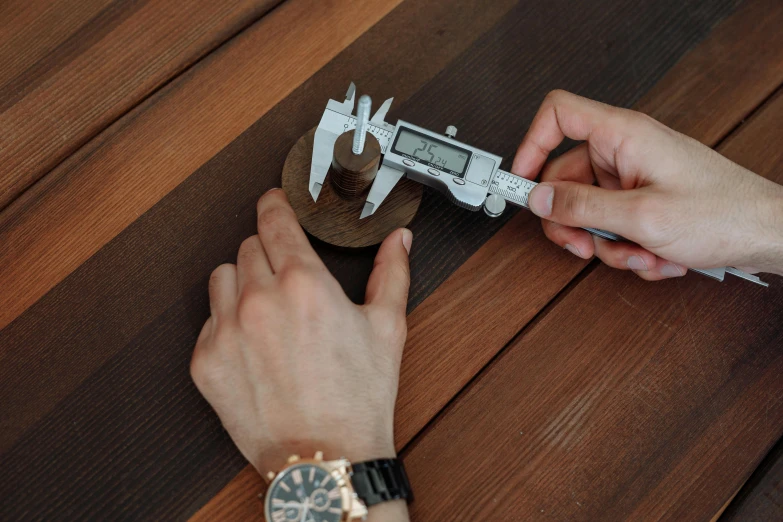 a close up of a person holding a caliper, by Alexander Fedosav, pexels contest winner, wooden table, ultra accurate, round format, high details photo