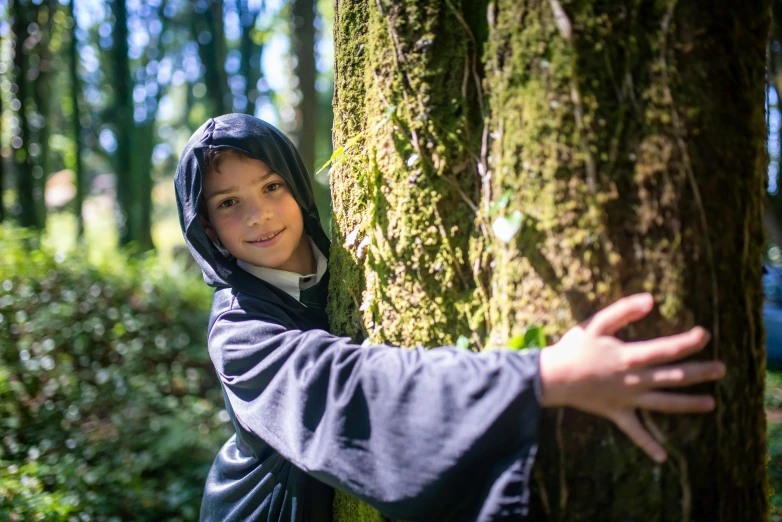 a person leaning against a tree in a forest, inspired by Arthur Hughes, little boy wearing nun outfit, avatar image