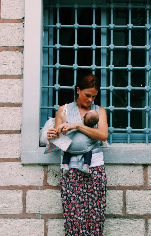 a woman holding a baby in front of a window, by Lucia Peka, pexels, wearing a vest top, in an alley, italy, cloth wraps