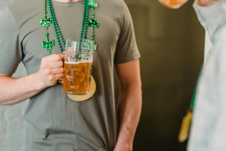 a man drinking a beer at a st patrick's day party, by Carey Morris, pexels, tan skin a tee shirt and shorts, wearing several pendants, promotional image, glassware