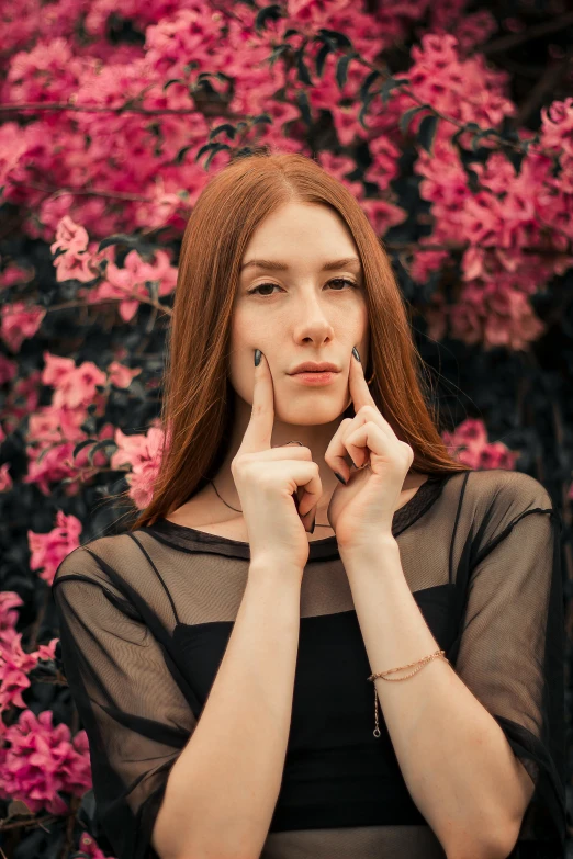 a woman standing in front of a bush of pink flowers, by Julia Pishtar, pexels contest winner, renaissance, hands on face, karen gillan, black dress : : symmetrical face, medium format