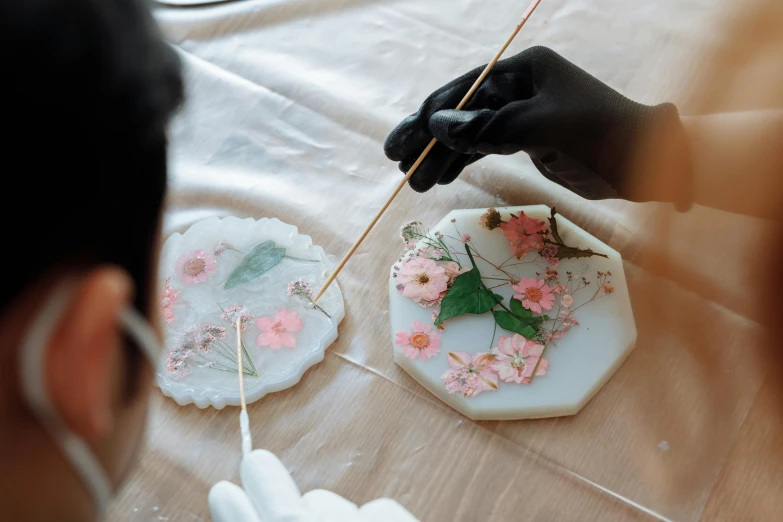 a close up of a person holding a stick, a silk screen, trending on pexels, pressed flowers, molten plastic, tabletop, white wax