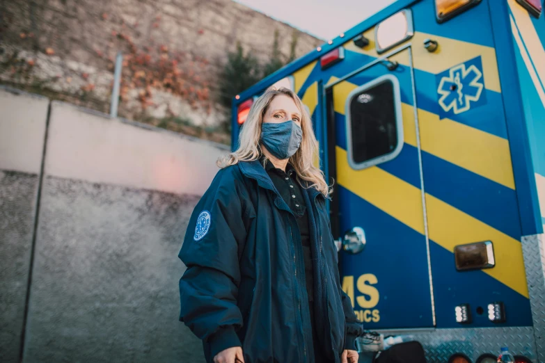 a woman in a face mask standing in front of an ambulance, pexels, renaissance, blue uniform, beeple and james jean, erin moriarty, against dark background