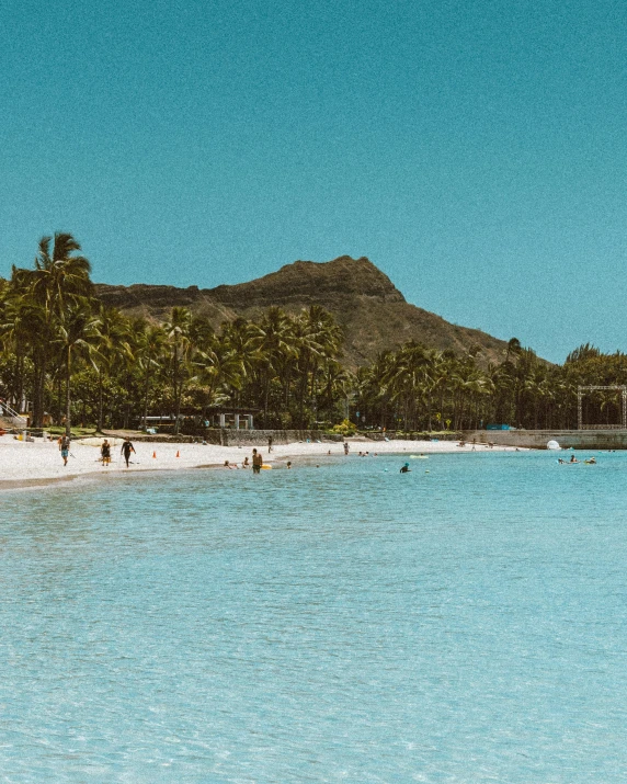 a group of people standing on a beach next to a body of water, coconut trees, blue water, waikiki beach, teal aesthetic