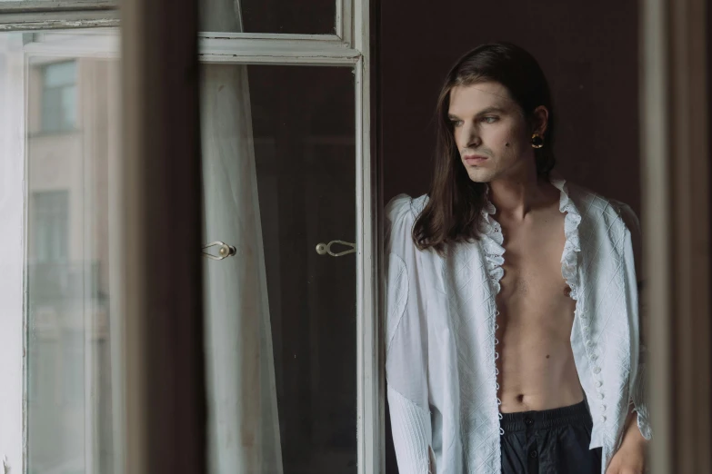 a shirtless man standing in front of a window, an album cover, inspired by Elsa Bleda, unsplash, renaissance, wearing lab coat and a blouse, delicate androgynous prince, portrait fashion model, ukrainian