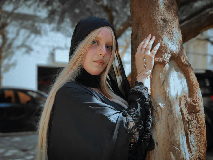 a woman that is standing next to a tree, an album cover, inspired by Modest Urgell, pexels contest winner, renaissance, black hood, modeling photograph kerli koiv, realistic cosplay, orthodox saint