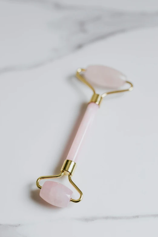 a rose quartz roller on a marble surface, by Julia Pishtar, face accessories, spoon, 12, y2k”