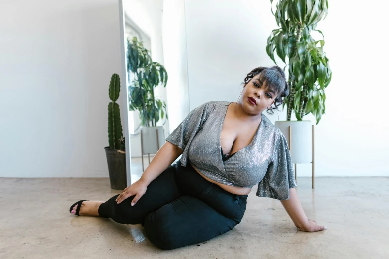 a woman sitting on the floor in front of a mirror, trending on pexels, alluring plus sized model, wearing a cropped top, shiny silver, large)}]