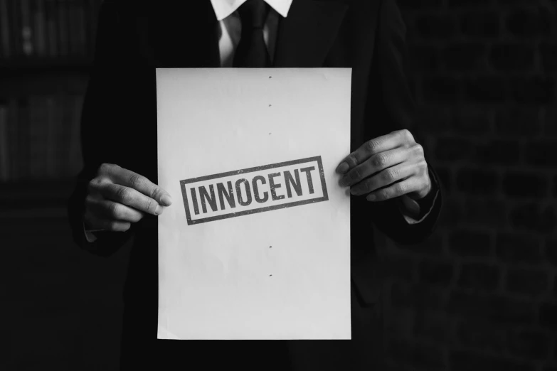 a man in a suit holding a sign that says innocent, an album cover, by Niko Henrichon, pixabay, incoherents, monochrome, violence, patent, background image