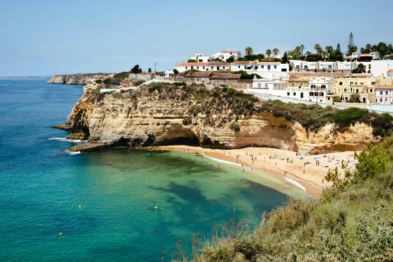 a group of people standing on top of a beach next to a body of water, renaissance, cliffside town, rocha, travel guide, profile image