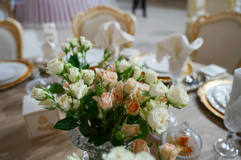 a close up of a vase of flowers on a table, pexels, rococo, crown of peach roses, cream and white color scheme, dining table, far view