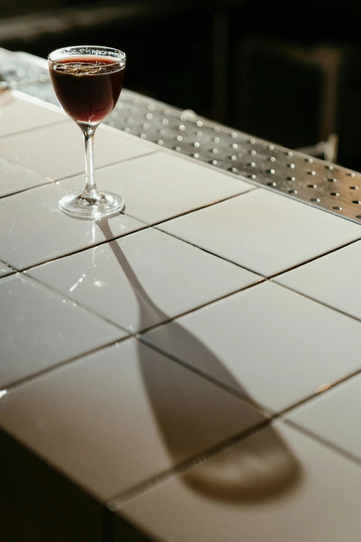 a glass of wine sitting on top of a counter, a mosaic, walking down, made of all white ceramic tiles, up-close, bar