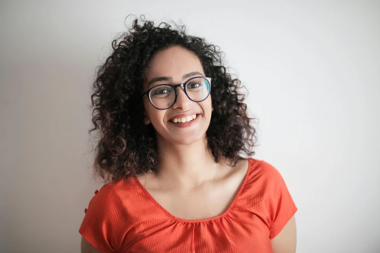 a woman with glasses smiling at the camera, pexels contest winner, hurufiyya, curls on top, amr elshamy, plain background, avatar image