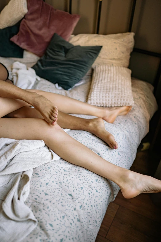 a woman sitting on top of a bed next to pillows, by Elsa Bleda, unsplash, looks like varicose veins, woman holding another woman, exposed thighs, spasms
