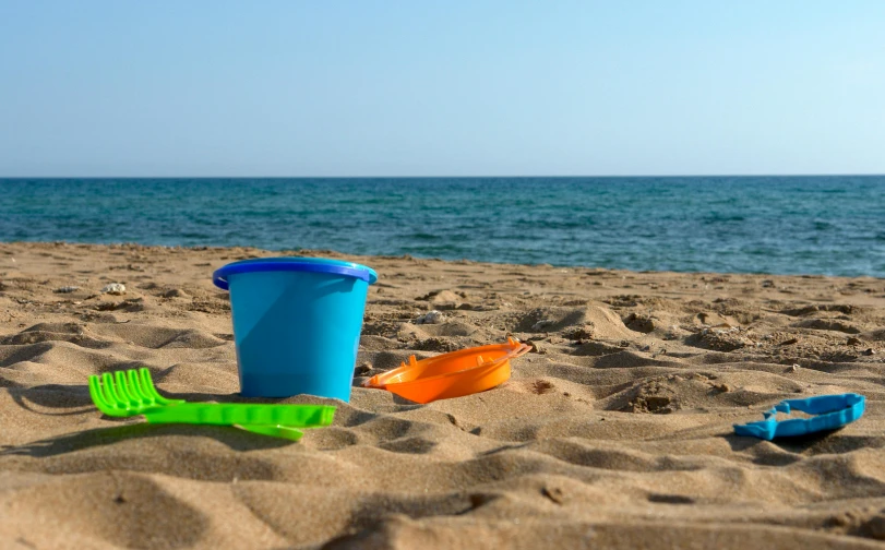 a blue bucket sitting on top of a sandy beach, at the sea