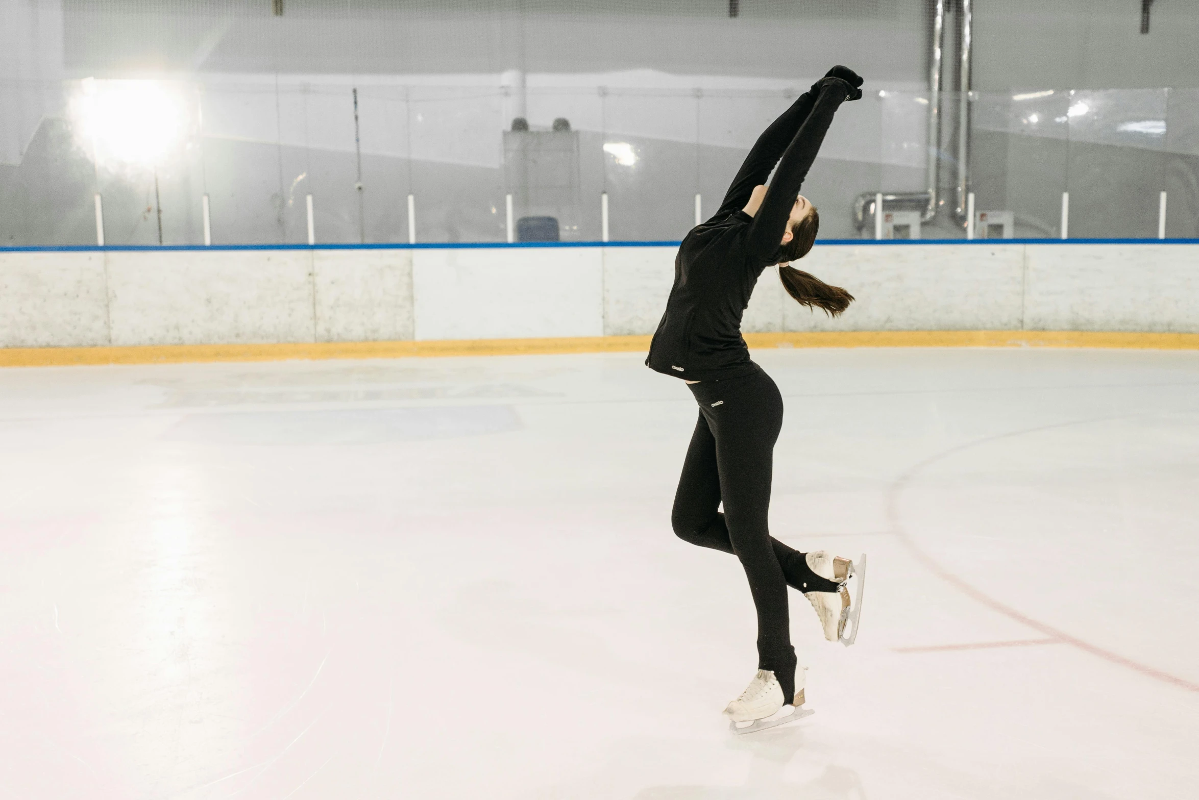 a female figure skating on an ice rink, pexels contest winner, arabesque, wearing a tracksuit, back pose, low quality photo, full body image